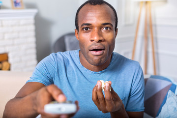 So tasty. Nice pleasant handsome man holding popcorn and eating it while watching TV program