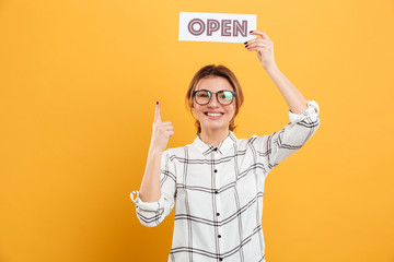 Portrait of attractive woman in eyeglasses pointing finger on open sign holding above head and...