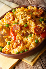 Paella Valenciana with meat, sausage chorizo, vegetables and spices close-up in a bowl. vertical