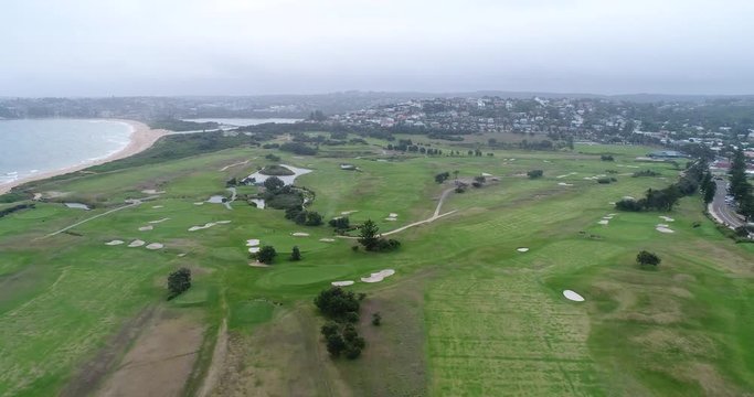 Green golf course and club filed on Long Reef headland in Sydney. Aerial view flying over holes, traps, tracks in proximity of pacific ocean and mona vale beach.
