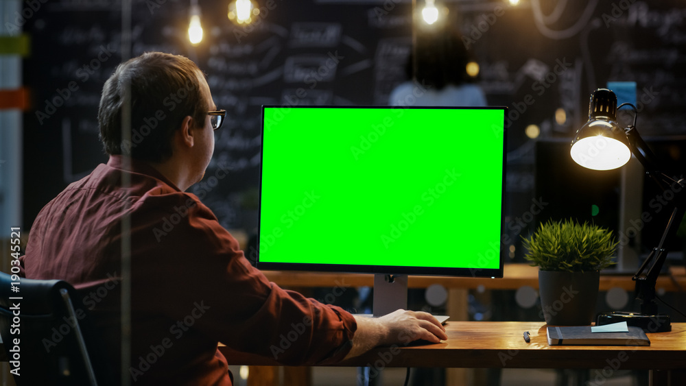 Poster office employee at his desktop works on a mock-up green screen personal computer. over the shoulder 