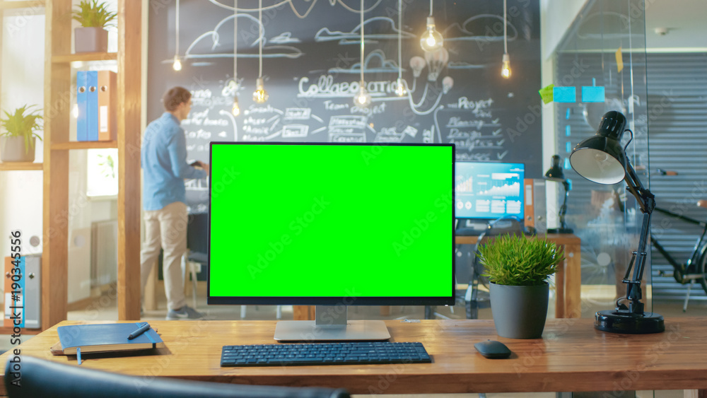 Poster personal computer with mock-up green screen monitor stands on the office desk, in the background man