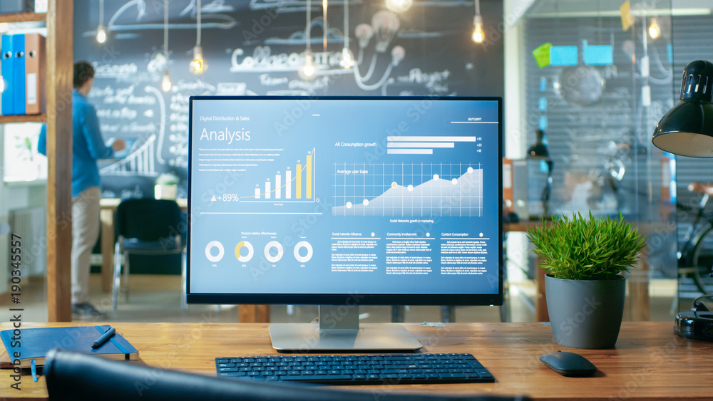 Poster Personal Computer with Mobile Application Design Showing on the Monitor Stands on the Office Desk, In the Background Man Working in the Daytime Office Environment.