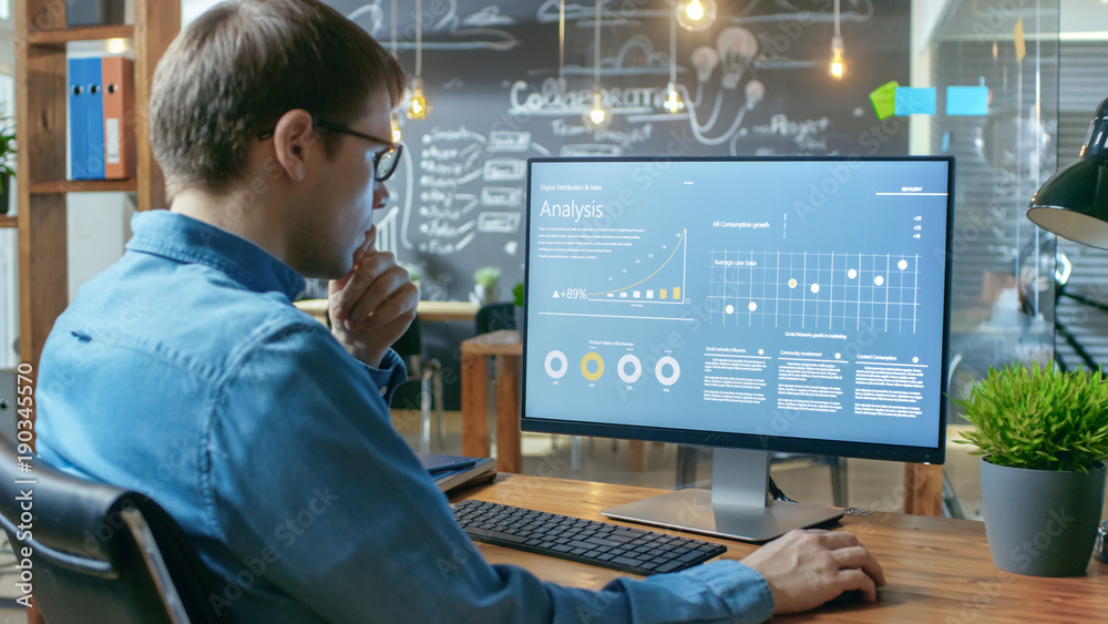 Aufkleber financier works on a personal computer showing statistics, graphs and charts. in the background his 