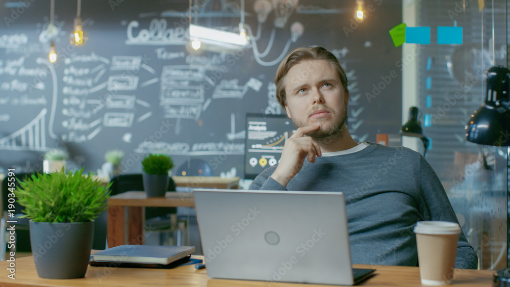 Poster Handsome Young Office Employee Thinks on a Problem Solution While Working on a Laptop Computer. He's Working in the Creative Stylish Office.