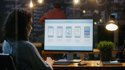 Beautiful Female Mobile Video Gaming Application Developer Works at Her Desk on a Personal Computer. In the Background Her Colleague in the Creative Office.
