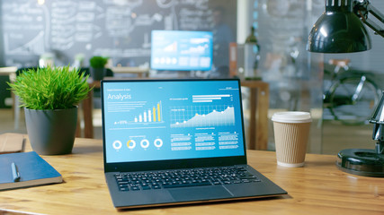 Personal Computer with Statistical Data, Graphs and Charts on Display. In the Background Stylish Creative Office at Daytime.