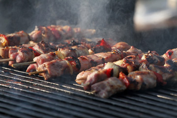 Kebab on wooden skewers on grill. Shashlik or shashlyk – meat skewers on grill outside. Shish kebab on a barbecue. Roast meat on BBQ. Selective focus through smoke.