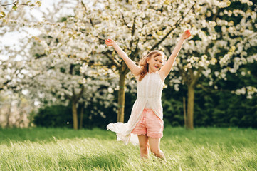 Pretty little kid girl playing in spring blooming garden