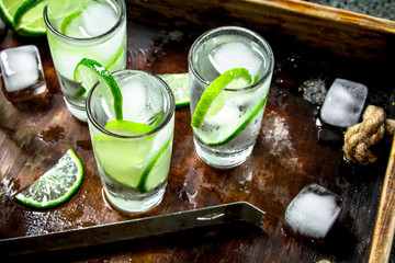 Vodka with lime and ice on a wooden tray.
