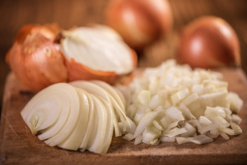 close up of chopped, sliced, halved and whole onion on wood table 