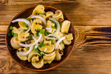 Ceramic plate with canned mushrooms on wooden table. Top view