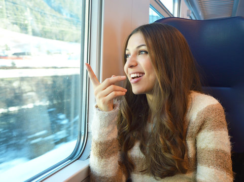 Happy smiling woman travelling in train and pointing a place through the window