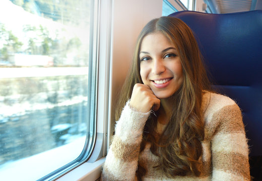 Smiling girl travelling in train with winter snow landscape out of the window looking at the camera