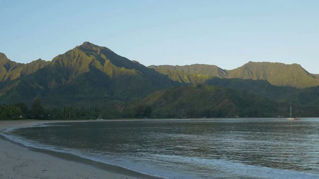 Locked down view of Hanalei Bay, Kauaii, Hawaii, shortly after sunrise, as early morning light strikes surrounding mountain peaks.