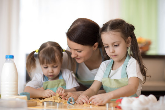 Happy loving family mother and daughters are preparing bakery together. Mom and children are cooking cookies and having fun in the kitchen. Homemade food and little helpers.