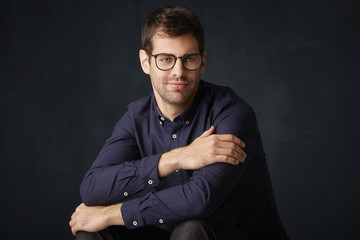 Young businessman portrait. Portrait shot of a relaxed young man sitting at dark background and smiling. 