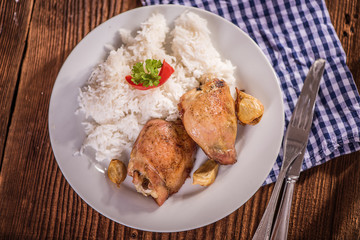 chicken tights upper leg on white plate with rice on wood table. 
