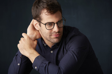 Young man deep in thought. Studio portrait of handsome young man looking away thoughtfully and deep in thought while sitting at dark background. 