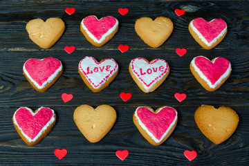 Decorated of Valentines Day. Many small cookies with glaze, in the shape of a heart with the inscription "love" on it, lie in a row On a dark wooden background. Concept Valentines days food.
