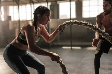 Gordijnen Young woman working out with battle ropes © Jacob Lund