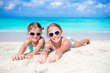 Close up little girls on sandy beach. Happy kids lying on warm white sand