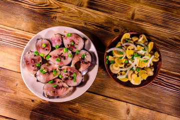 Sliced scomber fish and canned mushrooms with green onion on a ceramic plates on wooden table