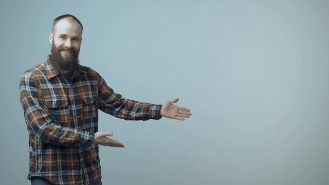 Satisfied bearded man dancing joyfully and pointing at blank copy space for text or product while showing approving gestures