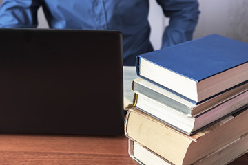 Books and laptop on the desktop. A man sits behind a desktop.