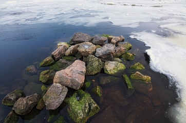White ice and snow pieces with several stones in river coast water in cold winter morning