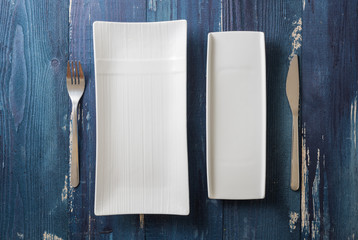 White rectangular Plates with fork and knife on blue wooden background