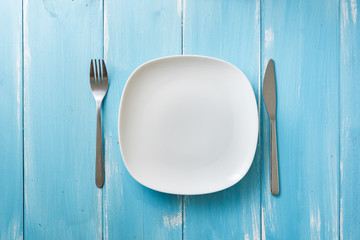 White Plate on blue wooden background with utensils