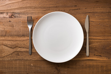 White Plate on brown wooden background with utensils