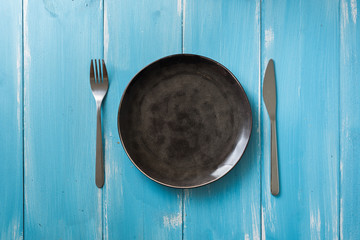 Black Plate on blue wooden background with utensils