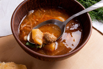 Close up view of clay plate and spoon with red beetroot soup or borsch on wooden background..