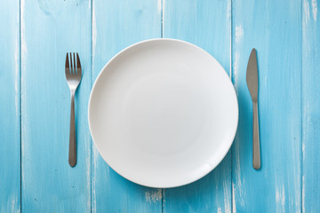 White Plate on blue wooden background with utensils