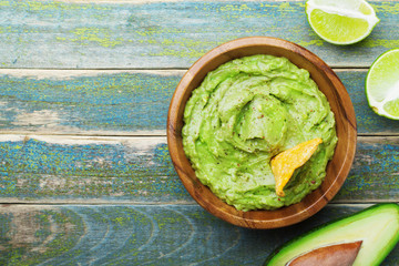 Green guacamole with  ingredients avocado, lime and nachos on wooden vintage table top view....