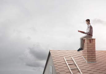 Handsome man on brick roof against cloud scape reading book