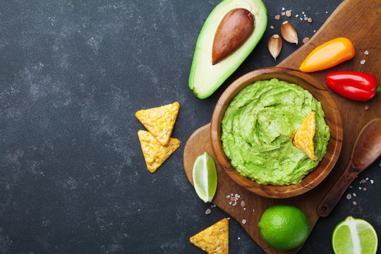 Guacamole dip with avocado, lime and nachos on black table top view. Copy space.Traditional mexican food.