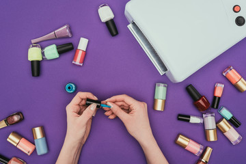 cropped image of girl painting nails isolated on purple