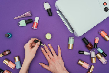 cropped image of woman painting nails isolated on purple