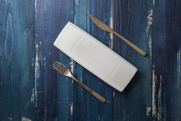 White rectangular Plate with fork and knife on blue wooden background