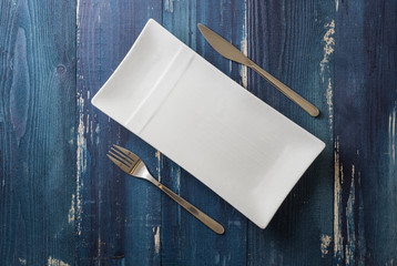 White rectangular Plate with fork and knife on blue wooden background