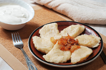 A plate with boiled dough vareniki with potato filling and fried onions. Near her bowl with sour...