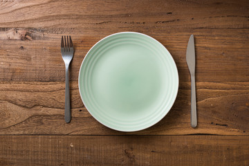 Green Plate on brown wooden background with utensils