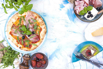 Italian Pizza with ruddy lush edges with prosciutto and olives. Green salad. Servian lunch, on a light background with punctuated spots. Free space for text or a postcard.