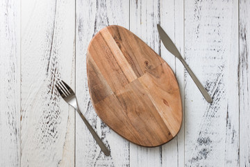 Oval cutting board with knife and fork on white wooden background