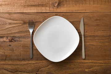 White Plate on brown wooden background with utensils