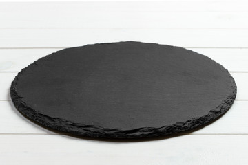 Black slate round stone on wooden background, top view, copy space