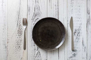 Black Plate on white wooden background with utensils